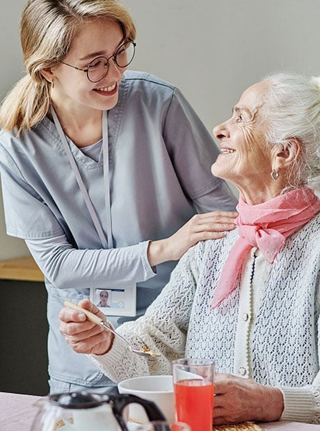 Caregiver talking to senior people and helping them while they eating at table