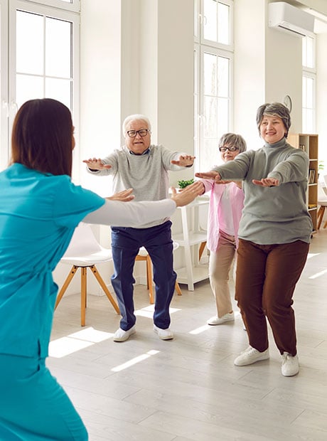 Senior group doing squat exercise with physiotherapist in gym