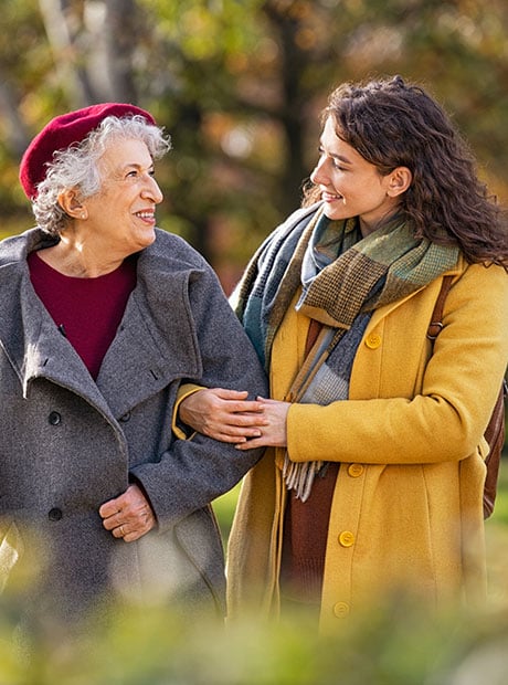 A senior woman walking with a friend in park during autumn.