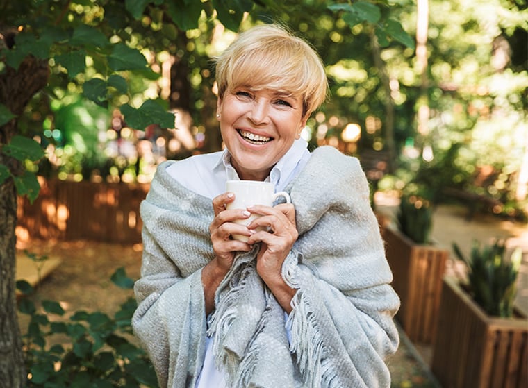 senior woman wrapped in a blanket outdoors while holding a mug