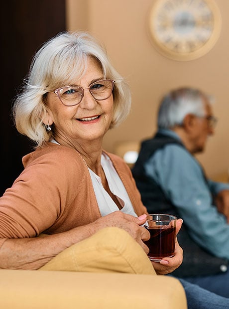 Smiling senior woman enjoys in cup of tea at nursing home and looks at camera