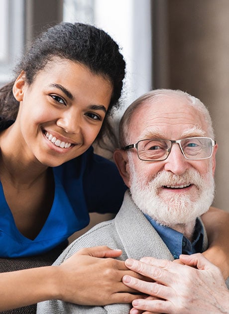 A smiling young doctor giving psychological help to an elder man during a home visit.
