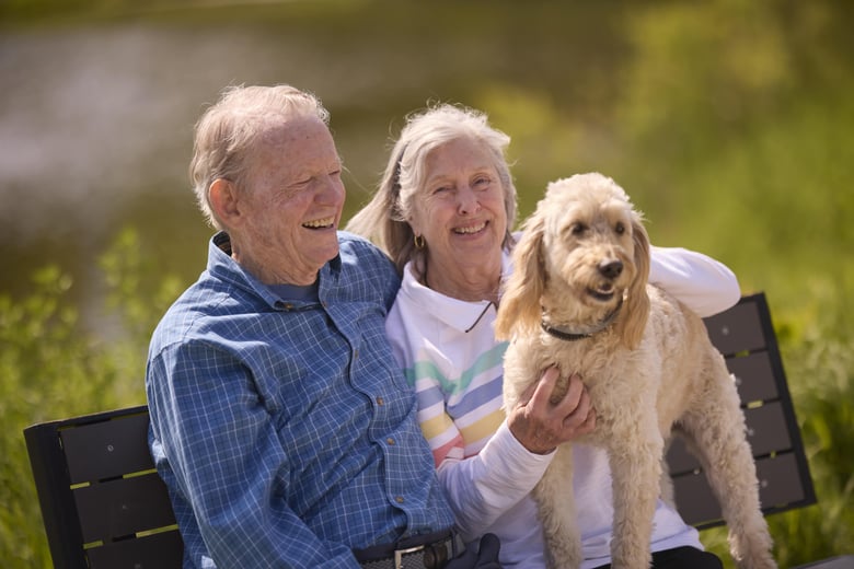 Happy couple sitting with their cute dog on a park bench