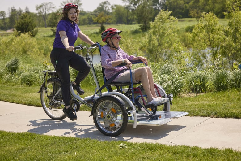Woman assisting riding a bike with a senior in a wheelchair
