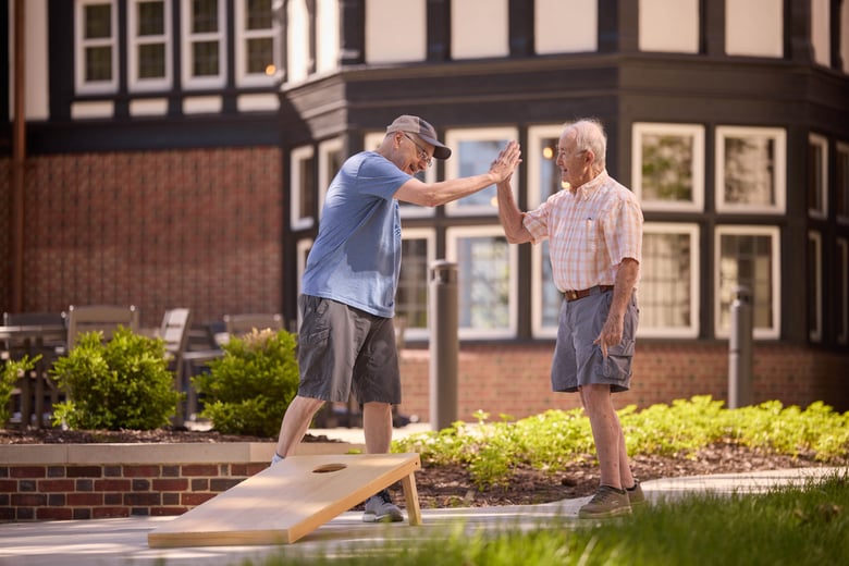 Two older men high-fiving and playing cornhole