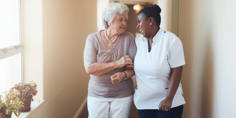 A happy female caregiver and an older adult woman walking together.