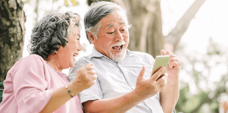 Joyful older couple looking at a smartphone outdoors.
