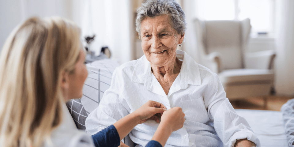 An at-home caregiver helping an older adult woman get dressed.