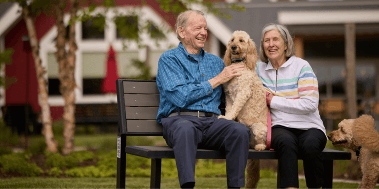 A happy senior couple sitting on a bench with their dog